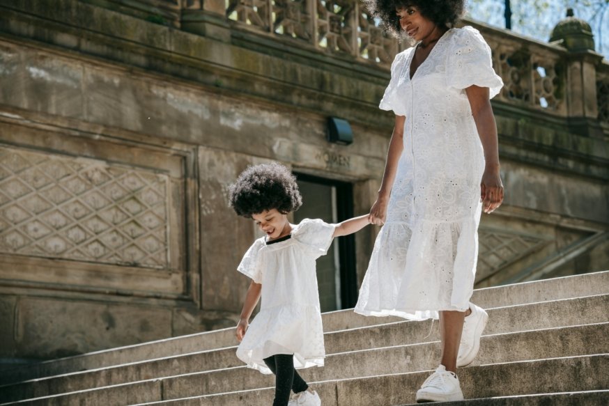 A joyful mother and daughter in white dresses walking down stairs outdoors.